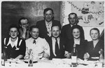 Administrators of the Wels dsiplaced persons' camp and the teachers of the Hebrew language school pose for a group portrait by a table in a decorated classroom.