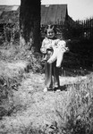 Portrait of Kitty Weichherz standing in a garden with her doll.