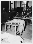 Prosecution witness Wolf demonstrates positions prisoners assumed for punishment on the whipping block in Dachau.