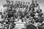 Group portrait of the employees of the Lodz ghetto post office holding a sign in the shape of a Star of David.