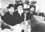 A group of Orthodox men gather around a festive table with candles in what [is probably the Zeilsheim displaced persons' camp].