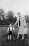 A German-Jewish mother takes her son for a walk through a grassy field.