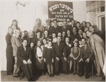 Groups portrait of survivors of the Biala ghetto in front of a Yiddish sign that reads, "Biala Ghetto, the first day of Sukkot 1942.
