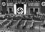 Formations of SA bicycle troops walk their bicycles past Adolf Hitler at a rally.