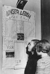 Two Jewish DP children read a newspaper posted on the wall of the Jewish (Deutsche Juedische Jugend) school at the Berlin Chaplains' Center.