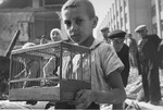 A young boy, Zygmunt Askienow, holds the cage containing his pet canary that he rescued from the ruins of his family's home in Warsaw.