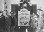 Jewish DPs in Cremona, Italy, gather around a plaque memorializing Jews who were killed by the Nazis during the suppression of the Warsaw ghetto uprising.