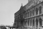 Latvian civilians walk past the Riga city hall, which was damaged in a German air raid.