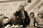 An unidentified man addresses the audience in a P.H.H.