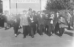 Yeshiva students march with Torah scrolls along a street in the Zeilsheim displaced persons camp, on their way to greet David Ben-Gurion during his official visit to the camp.