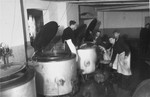 Work in the Zeilsheim camp kitchen pour food from large vats.