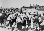 Jewish women from Subcarpathian Rus who have been selected for forced labor at Auschwitz-Birkenau, march toward their barracks carrying bed rolls after disinfection and headshaving.