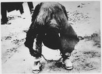 A male inmate of the Stara Gradiska concentration camp bends over to adjust his leg irons.