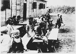 Children sit on benches outside a barracks in the Gornja Rijeka concentration camp.
