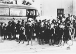 A group of young Serbian children from the Kozara region who are dressed in Ustasa uniform, are assembled next to a bus in the Stara Gradiska concentration camp.