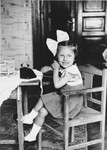 A young Jewish girl sits at a table talking on a toy telephone.