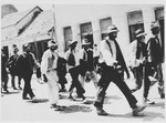 A group of men who have been rounded up for deportation, are marched out of town.