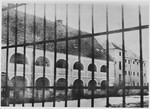 View through a tall fence of prisoner barracks in the men's camp at the Stara Gradiska concentration camp.