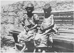 Two emaciated children sit outside on a bench in the Jastrebarsko concentration camp.