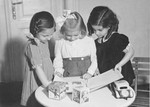 Three Jewish preschool girls look at a picture book in a playroom.