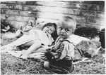 Two young children rest on a layer of straw on the floor of a barracks in the Sisak concentration camp.