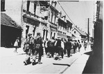 [Probably Serbian villagers from the Kozara region who have been rounded-up for deportation, marching in a column under Ustasa guard through the streets of a town.]
