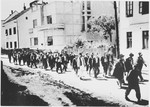 [Probably Serbian villagers from the Kozara region who have been rounded-up for deportation, marching in a column under Ustasa guard through the streets of a town.]