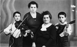 Two boys playing musical instruments pose for a studio portrait with their mother and grandmother.