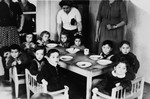 Kindergarten children gather around a table to eat lunch in the Wasseralfingen DP camp.