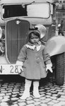 The young step-sister of Natan Slepian poses next to a large automobile.