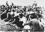 Ustasa guards move among a large group of Serbian villagers who are seated on the ground near the entrance to the Jasenovac concentration camp.