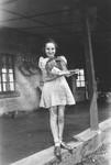 A young Jewish refugee girl stands in front of her farmhouse near Limuru, Kenya (Kiambu district), holding a cage of parakeets.