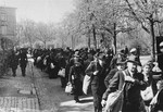 Jewish deportees, carrying a few personal belongings in bundles and suitcases, march through town along the Hindenburgstrasse from the assembly center at the Platzscher Garten to the railroad station.