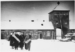 A group of female survivors of Auschwitz-Birkenau trudge through the snow through as they depart from the camp through the main gate.