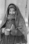 A Jewish child wearing a blanket, holds a cup and a piece of bread in the Kielce ghetto.