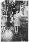 Three Jewish teenage girls wearing armbands pose by a tree in a forest in Olkusz.