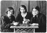 Studio portrait of three young women posing around a chessboard.