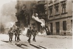 SS troops walk past a block of burning housing during the suppression of the Warsaw ghetto uprising.