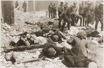 SS troops search through scattered personal belongings as a small number of Jewish resistance fighters lie on the rubble nearby.