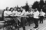Members of the SS Helferinnen (female auxiliaries) sit on a fence railing in Solahuette as Karl Hoecker passes out bowls of blueberries.