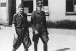 Two SS officers walk together past a building.

The original caption reads "Nach der Ausfahrt" (after the outing [exiting the mine]).