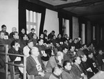 View of the defendants in the Dachau trial wearing identifying number tags seated in the dock.
