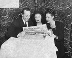 Three French singers and dancers huddle around an open French newspaper.
