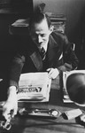Portrait of a German-Jewish immigrant sitting at his desk reading a newspaper.