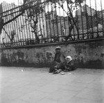 A destitute man and child sit against a wall on a street in the Warsaw ghetto.