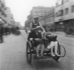 Two Jewish women ride in a rickshaw along a street in the Warsaw ghetto.