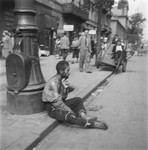 A destitute man sits on a curb in the Warsaw ghetto.