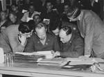 American military attorneys review a stack of documents while seated in front of the defendants during the Dachau war crimes trial.