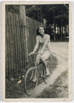 A teenage girl rides her bicycle down a dirt path next to a wooden fence.