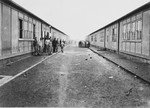 Survivors congregate on a road of the Dachau concentration camp flanked by barracks on either side.